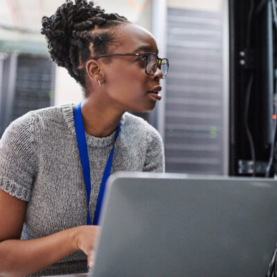 woman with glasses and a laptop in a technology server room