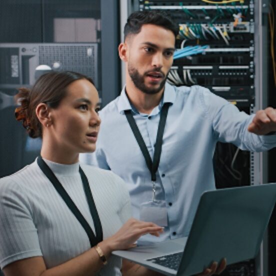 A pair of professionals, male and female, conversing with a computer, appearing to be solving a complex problem.